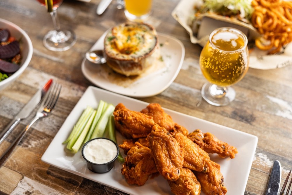 Buffalo wings and French onion soup on a wooden table at Dogtooth Bar and Grill