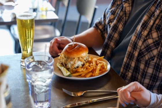 A burger and fries beside a tall pour of MudHen beer